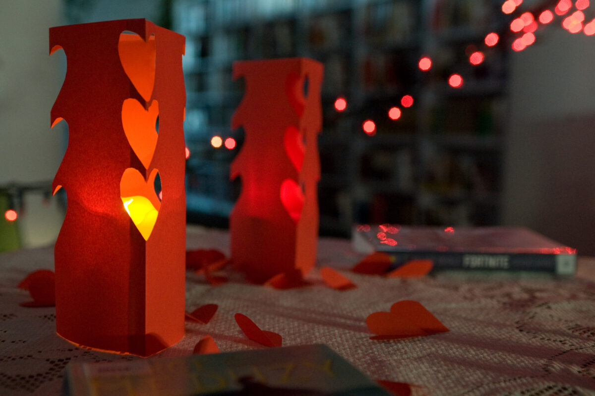 Wycięte czerwone lampiony z bloku rysunkowego, wzdłuż kominku wycięte serduszka a w środku świecąca się świeczka.
