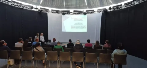 Uczestnicy spotkania siedzą na widowni w sali Poczytalni i słuchają prezentacji dotyczącej legalizacji pobytu oraz opieki zdrowotnej dla osób z doświadczeniem migracji.